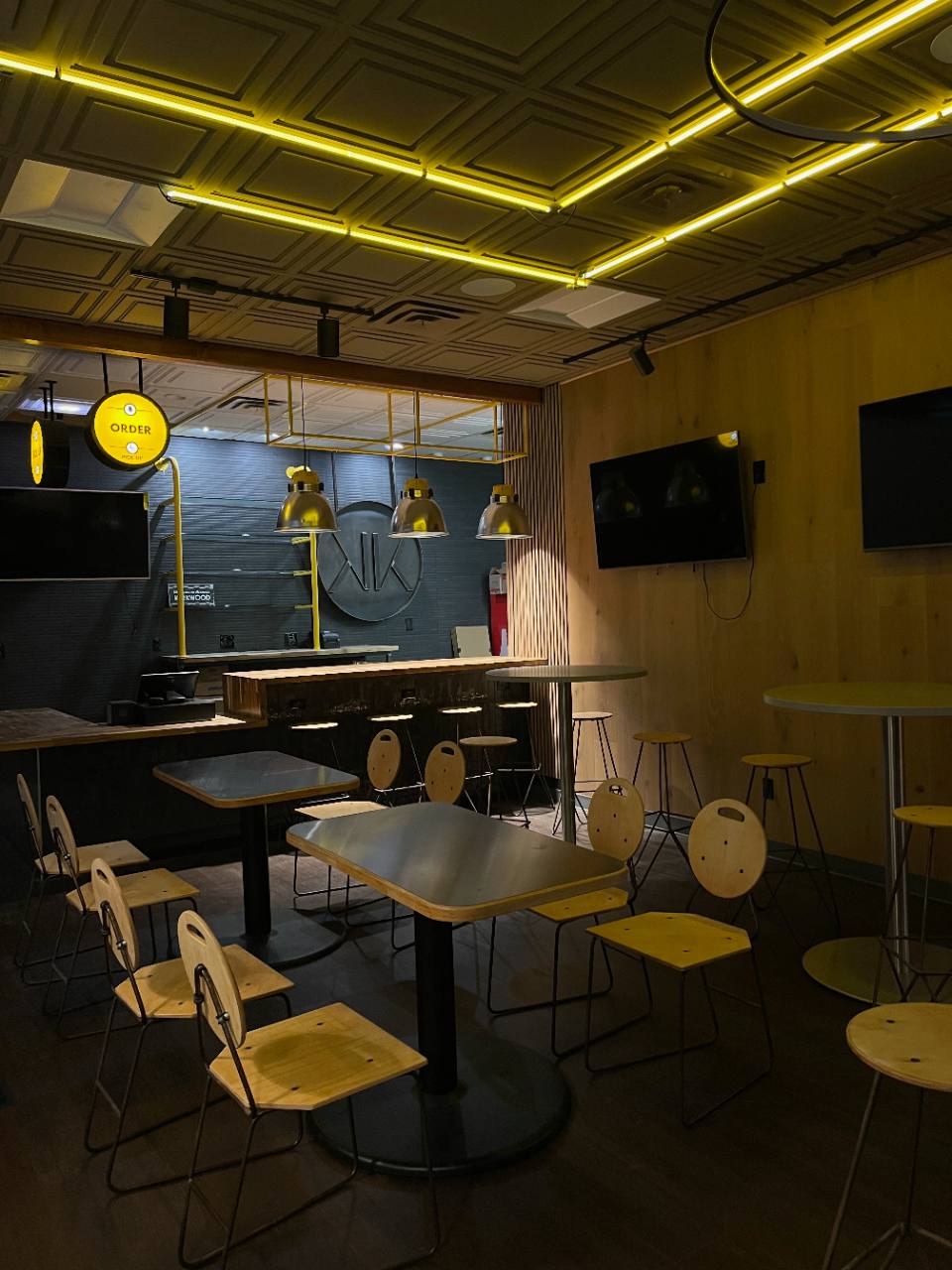 Commercial dining room interior with warm wood finishes, dark walls, and yellow ceiling lighting