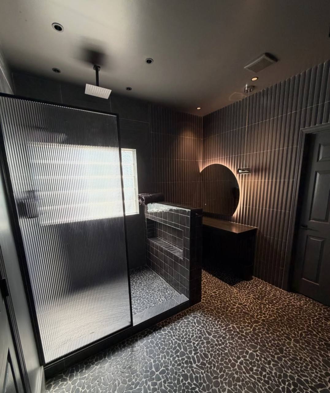 Dark spa bathroom with fluted glass shower and warm mirror lighting