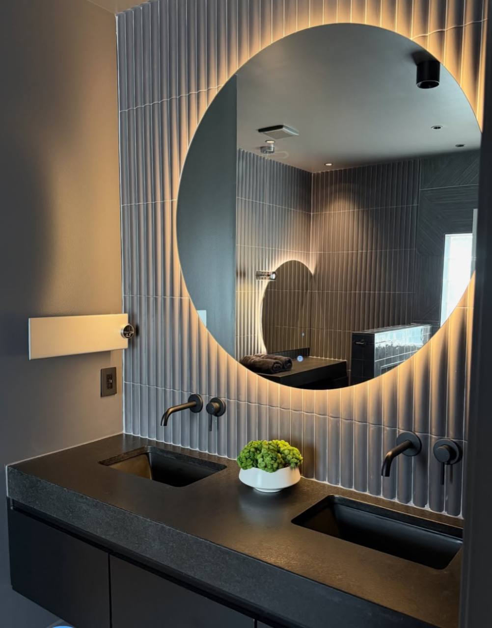 Modern vanity with round backlit mirror and dark stone counter